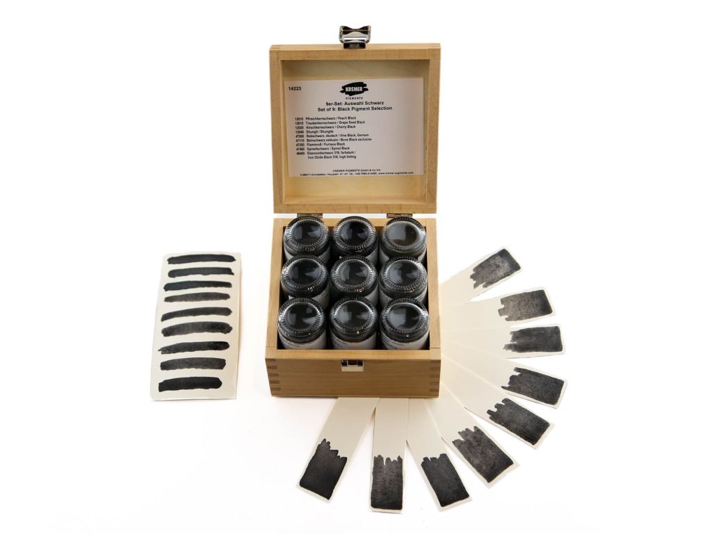 Black pigment set in wooden box with samples on paper fanned out on table.