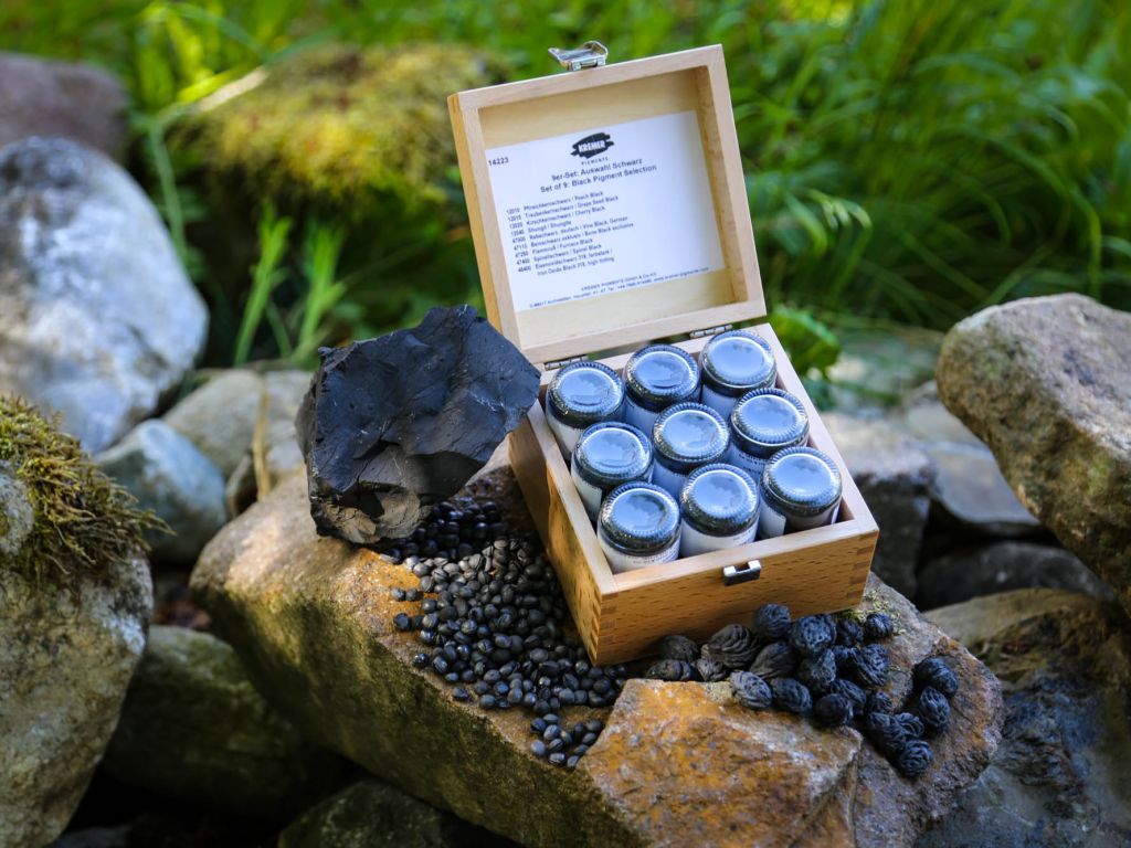 Wooden box with glass jars containing black berries on a stone surface with greenery in the background