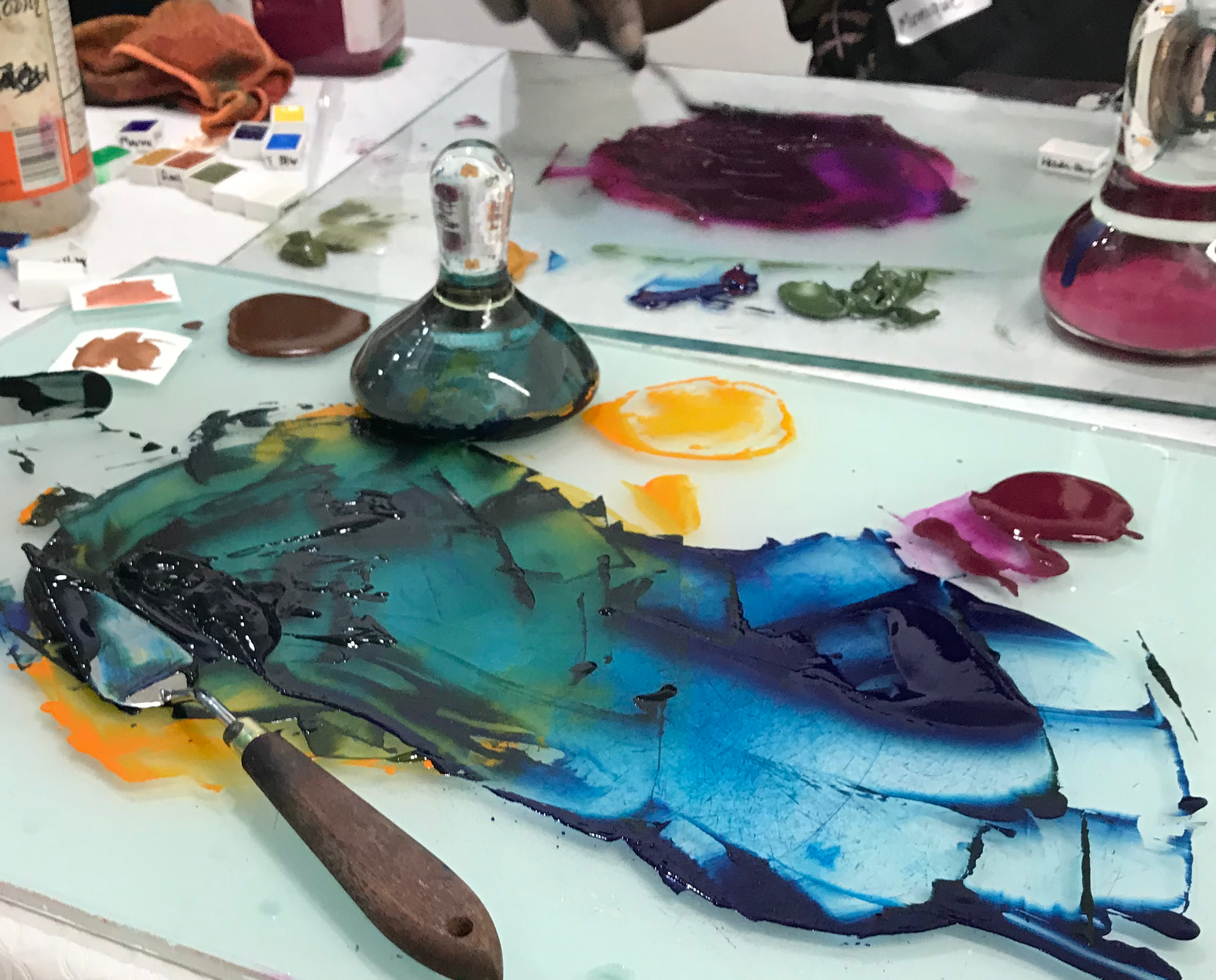 Artistic workspace with colorful paint swatches and a palette knife on a glass surface.